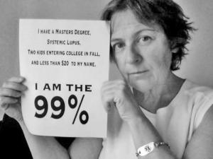 Black and white picture of a middle-aged white woman with short dirty-blond hair. She is wearing a white, sleeveless shirt and holding up a sign that says, "I have a Master's Degree, Systemic Lupus, Two Kids Entering College in Fall, and Less than $20 to my Name. I am the 99%.