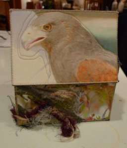 Top of treasure box has head and shoulders of a brown hawk with red wings. There are feathers on teh side of the box.